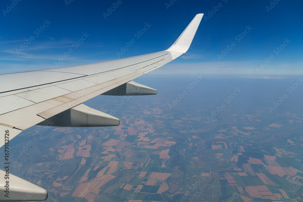 Fototapeta premium view from airplane window on wing and landscape below, horizon above planet and air haze, airplane view