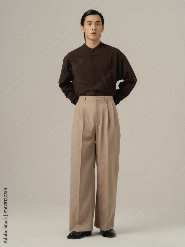 Obraz premium Young man in brown button-up shirt and beige pants standing in a modern indoor studio.