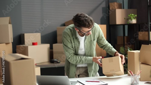 A man is standing in front of a stack of boxes, looking at one of them