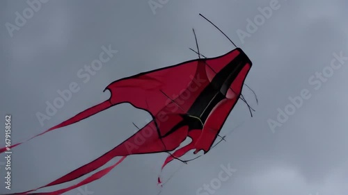Kite fluttering in stormy wind with sharply whipping tail against cloudy sky. Dynamic kite soaring showcases vibrant colors and motion, perfect for adventurous themes and video content.