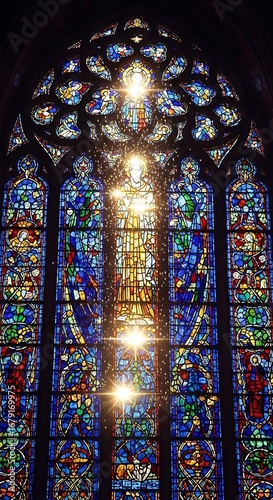 Vibrant Stained Glass Window with Religious Figures and Bright Sunbeams in a Historic Church or Cathedral