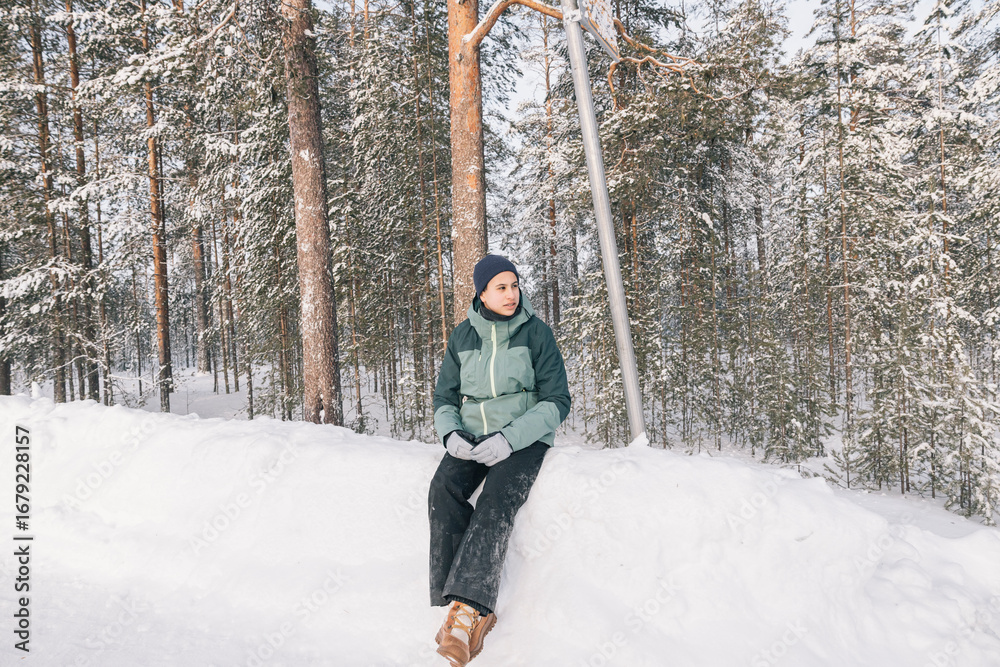 Naklejka premium Teenager girl wearing winter clothes sitting and relaxing in a snowy forest, enjoying the peace and quiet of nature