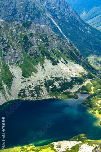 Deep blue lake at the base of steep rocky mountain slopes with green patches