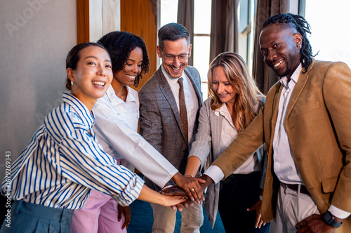 Portrait of diverse group of business people holding hands together in modern workplace looking at camera.
