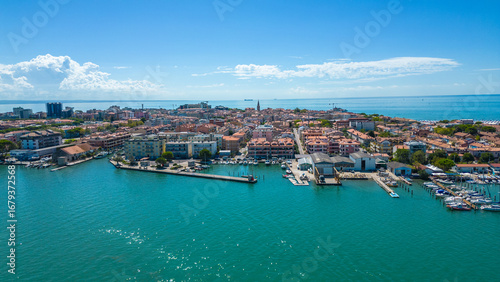 Obraz na płótnie Aerial view of kayaks and boats entering Grado, Italy, with turquoise Adriatic waters, a scenic bridge, and the historic seaside town in the background