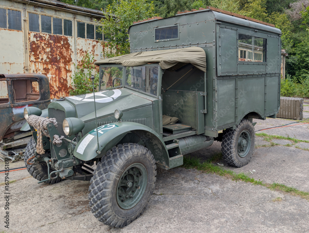 Fototapeta premium Vintage military truck parked near old industrial buildings in a rural setting
