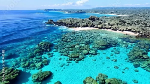 Serene coastal scene showcasing vibrant turquoise water, rocky shoreline, and lush green hills under a clear blue sky.