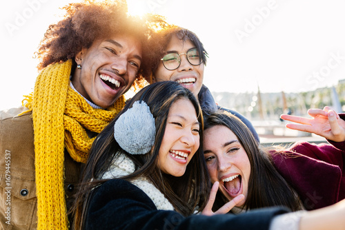 Happy young group of diverse people having fun taking selfie together with phone on winter at city street