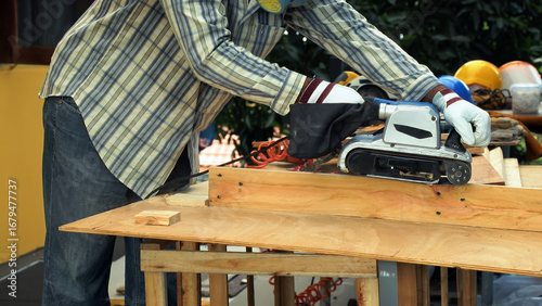 Foto Carpenter sanding wooden board with electric belt sander while wearing protectiv