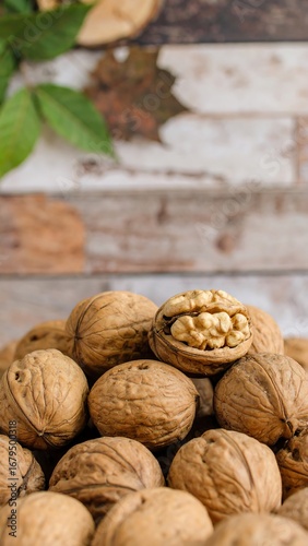 Close-up view of a pile of walnuts, showcasing their rich brown hues and textured shells, with one walnut cracked open to reveal the light-colored kernel inside.