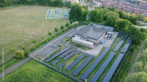 Aerial retreat small sustainable data center in the Netherlands with rooftop filled with solar panels, near housing, sports field, and small Dutch town