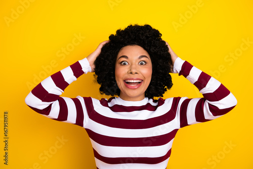 Happy young woman with curly black hair wearing a striped top, posing playfully against a vibrant yellow background