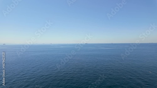 Calm ocean view with distant ships in clear blue skies near the coast during midday