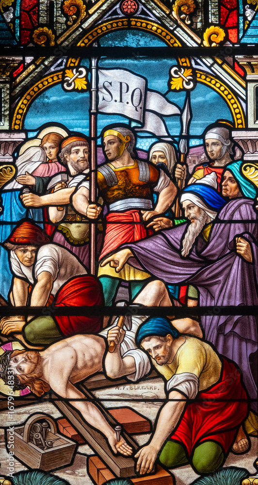 Fototapeta premium Stained glass (1914) of The Way of the Cross. Eleventh station: Jesus is nailed to the cross.