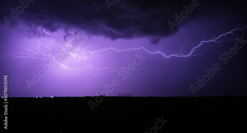 Fototapeta Naklejka Na Ścianę i Meble -  Vivid and dynamic display of lightning across a purple night sky above a dark landscape, showcasing nature's power and beauty.