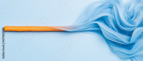 Vibrant orange stick is intertwined with flowing, silky blue strands, creating dynamic and artistic composition against light blue background. image evokes creativity and movement
