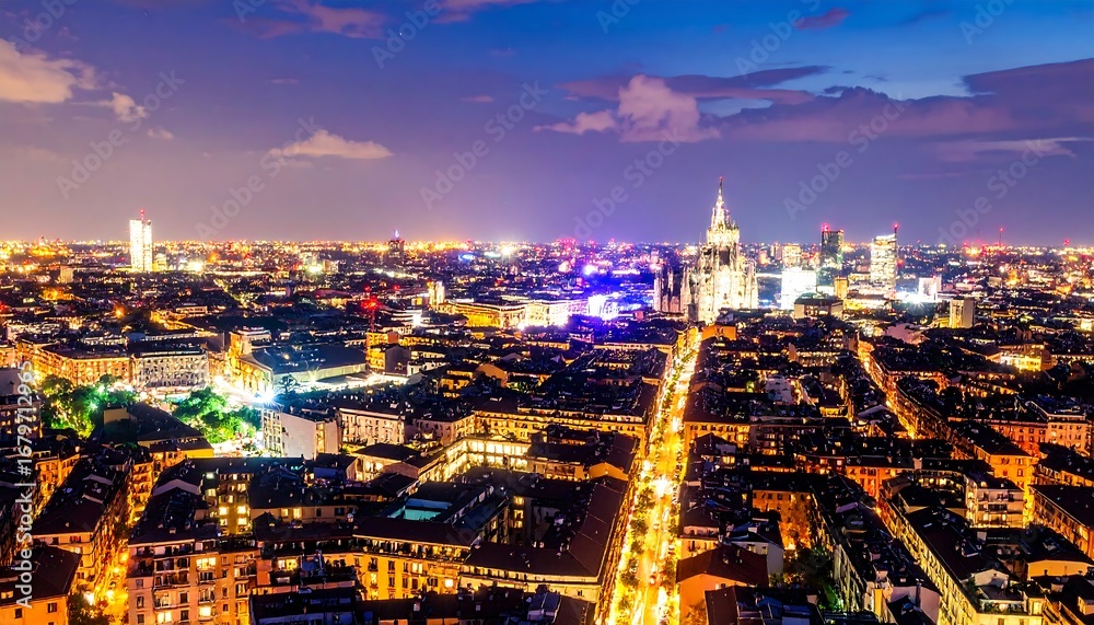 Naklejka premium A high-angle view of illuminated city streets and buildings at night, showcasing a vibrant cityscape with glowing lights.
