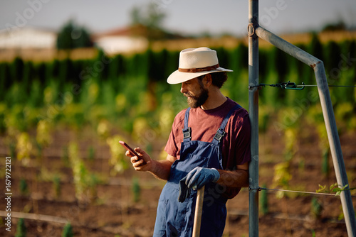 Fotografie Farm worker texting on cell phone while working in a field.
