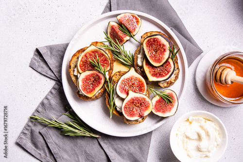 Freshly prepared fig and cheese platter garnished with rosemary on a white plate, accompanied by honey and creamy dip, showcasing a delightful culinary experience