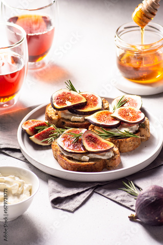 Freshly prepared fig and honey toast on a white plate, garnished with rosemary, accompanied by glasses of tea, showcasing a delightful culinary experience with vibrant colors