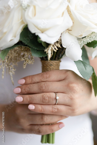 Manos de novia con anillo, sosteniendo ramo de flores. Boda