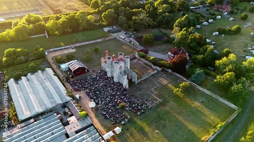 aerial drone shot wide high angle panning left tracking ancient old English Titchfield abbey ruins with large crowd of people in countryside in summer at sunset
