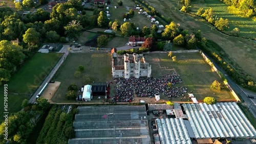 aerial high angle wide shot panning left tracking ancient old English Titchfield abbey ruins in countryside with large crowd of people at sunset in summer