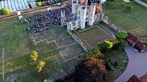 aerial drone shot cinematic quickly flying back and left away from ancient old English Titchfield abbey ruins in countryside with large crowd of peopler in summer at sunset