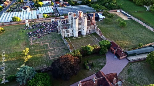 aerial drone shot diagonal view flying towards panning down over ancient old English ruins Titchfield abbey with large crowd of people at sunset in summer