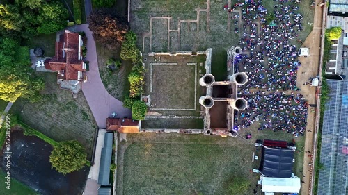 aerial drone shot Birds Eye view moving up over ancient English Titchfield abbey ruins with crowd of people in summer at sunset
