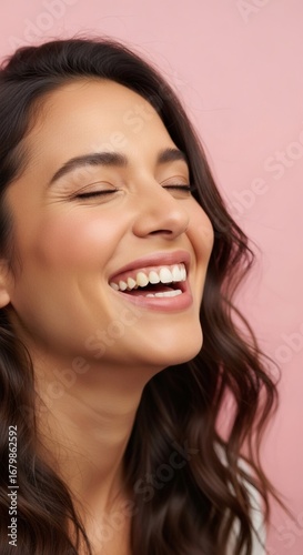 A smiling woman with closed eyes reveals her perfect white teeth on a pink background.