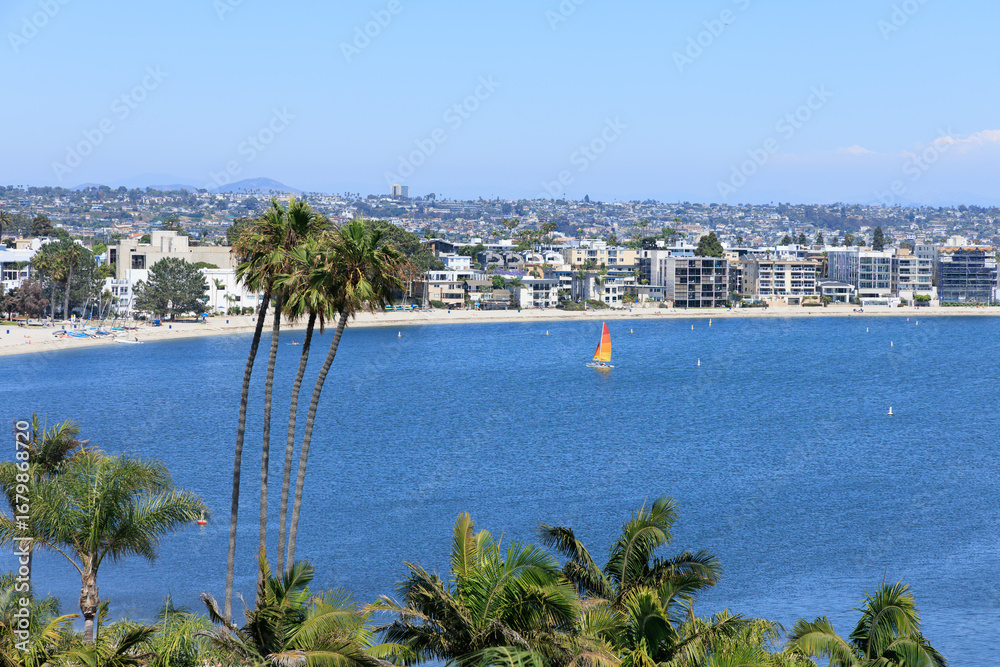 Fototapeta premium Birds-eye view of beachfront resorts, hotels and rental houses crowded at sandy edge of Sail Bay under summer blue sky with rare white clouds, San Diego, California