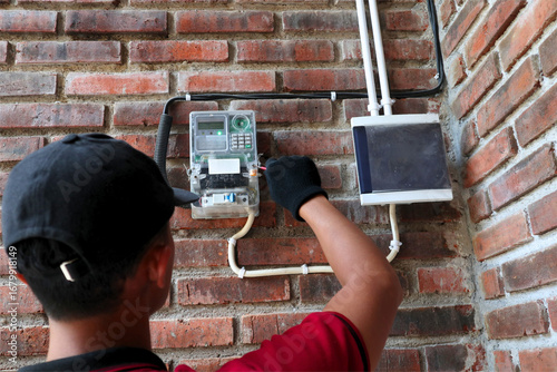 An Asian male electrical technician is checking an electricity meter (KWh Meter)