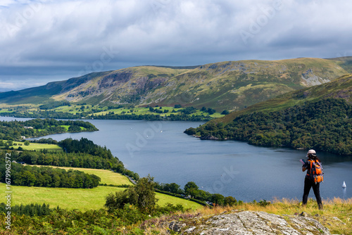 Woman standing on a fell overlooking the beautiful landscape of Ullswater lake.