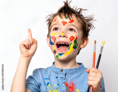 Wallpaper Mural Joyful boy covered in colorful paint, holding brushes, pointing up with an idea. Young artist's creative moment and bright expression. Torontodigital.ca