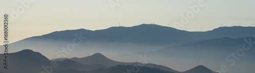 mountain landscape with fog and wind turbines on the tops for generating electricity