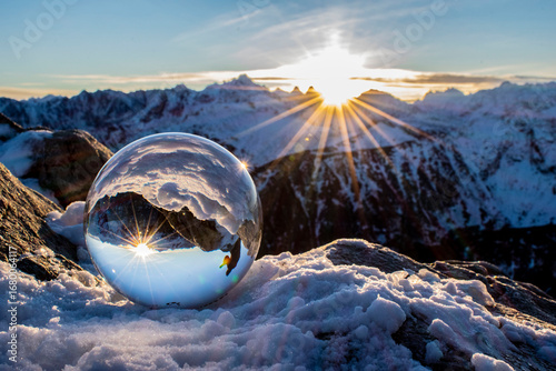 Foto a crystal ball with reflecting sunlight surrounded by winter mountains