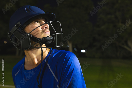 Adult man in blue baseball jersey and batting helmet standing on grass field, copy space