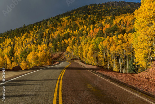 Autumn Road to Cripple Creek - Bright sun-lights shining through stormy clouds onto a winding mountain road on a colorful Autumn evening. CO State Highway 67, near Cripple Creek, Colorado, USA. 
