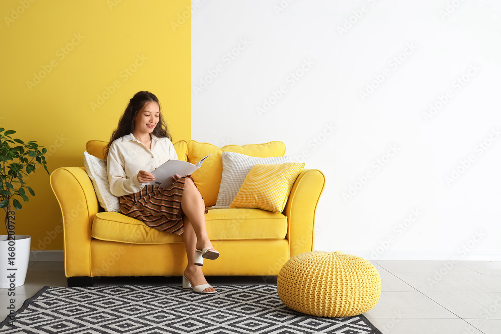 © Pixel-Shot - Young Asian woman reading magazine on yellow sofa near color wall