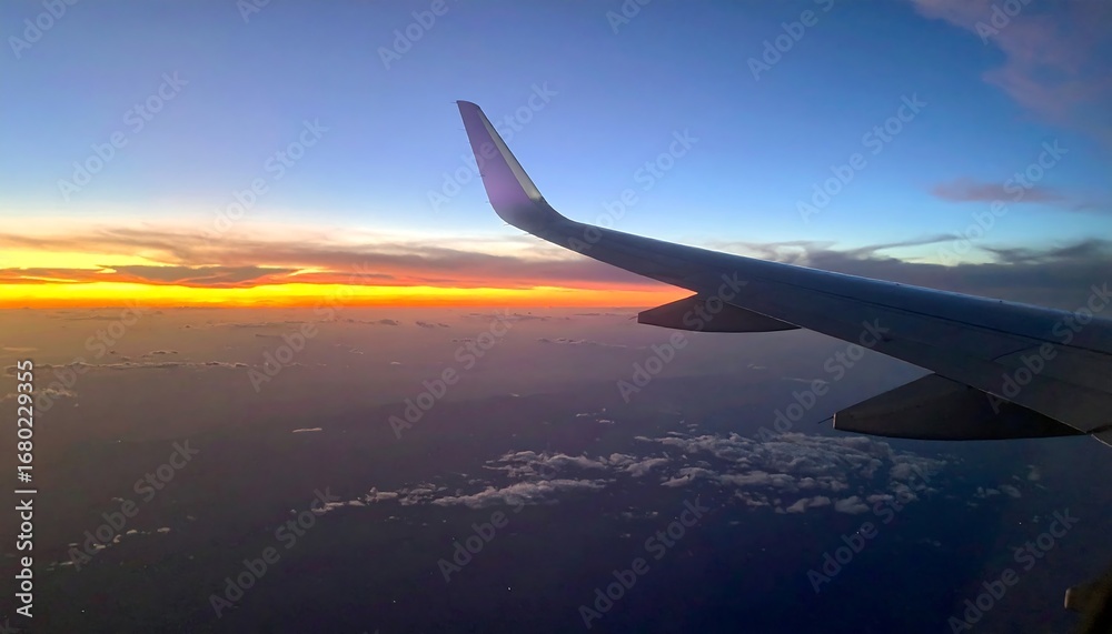 Obraz premium Airplane wing soars above cloudscape at sunset, vibrant orange and blue hues
