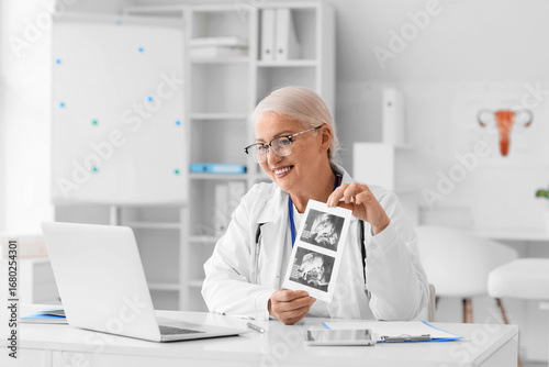 Female doctor with sonogram image and laptop giving online consultation in cl...