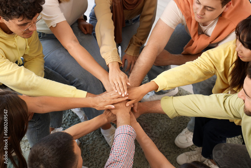 Young people putting hands together at group therapy session, top view