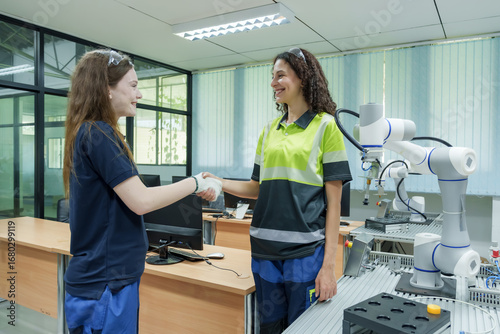 two female engineers shaking hands in smart factory robotics training lab showing successful collaboration and teamwork after completing hands-on robotic automation control session