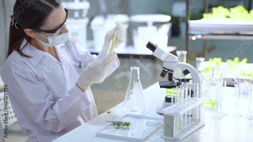 A female scientist wearing lab coat and mask conducts scientific experiments with microscope and test tubes in high tech lab.