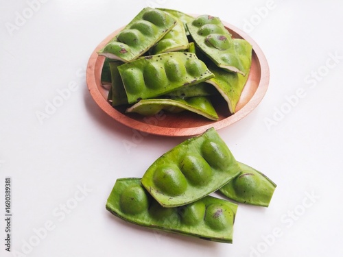 Foto Raw Petai (Parkia Speciosa) or Bitter Bean in a wooden plate on a white background