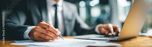 Close-up of person in business attire working on documents and a laptop