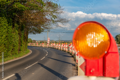Gelbes, unscharf fotografiertes Warnlicht auf einer Leitbake als Hinweis für eine Straßenbaustelle in einer unübersichtlichen Kurve mit scharfem Hintergrund