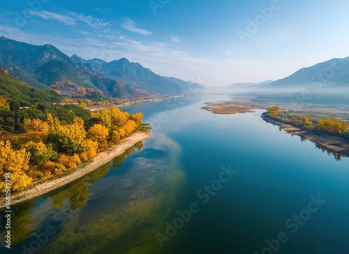 Aerial view of River with golden autumn foliage, blue water and misty orange mountains reflected in glass-like lake