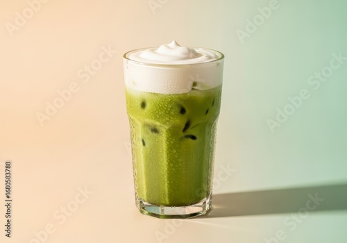 Iced matcha latte with cream top, clear tall glass, pastel café background